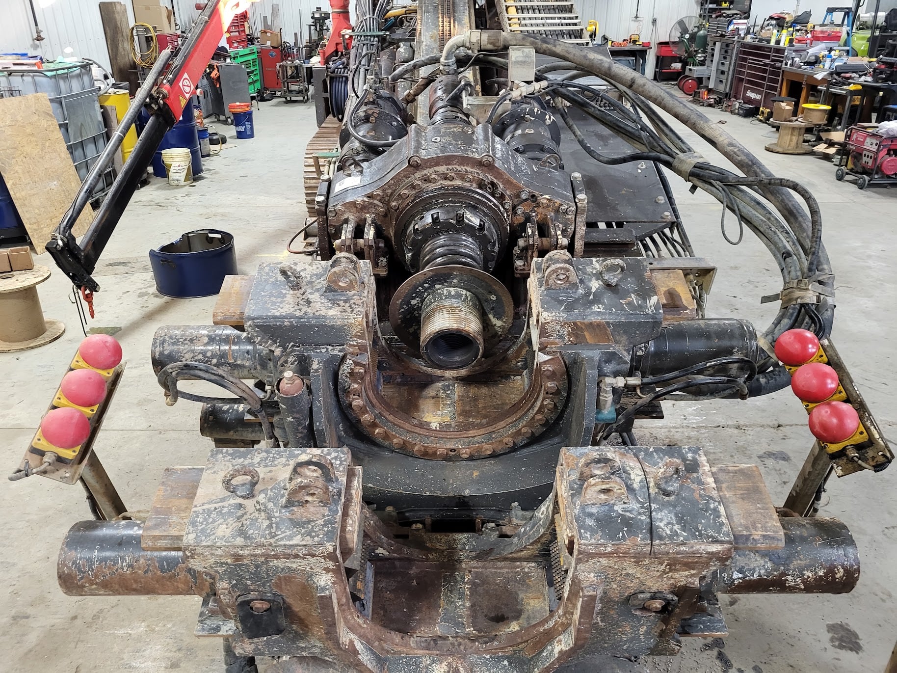 A drilling assembly in a workshop, with clamps, hoses and control levers around a central opening.